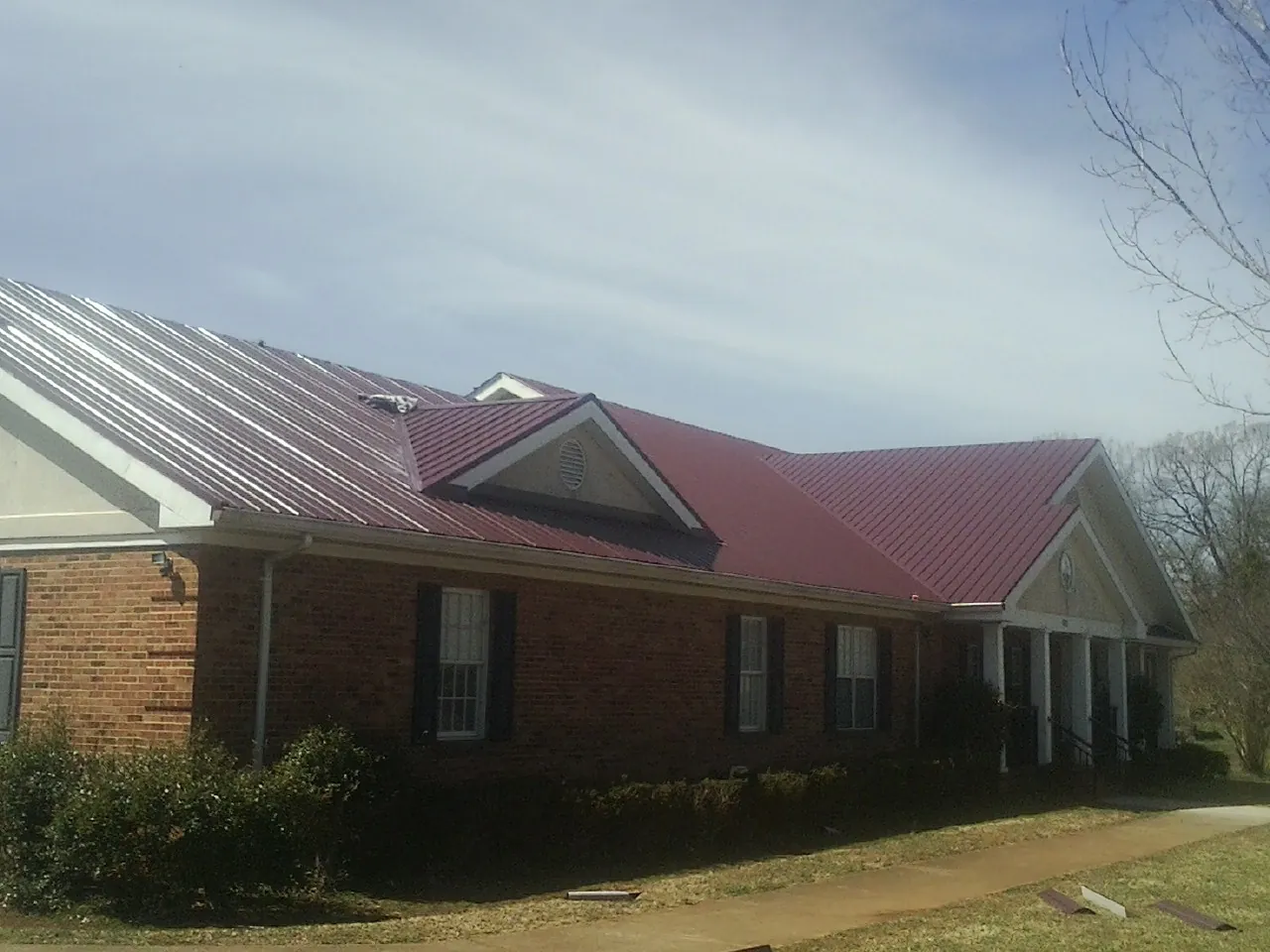 Red metal roof with gabled entries on a long brick building, from a Hail Damage Roof Repair job in South Lyon