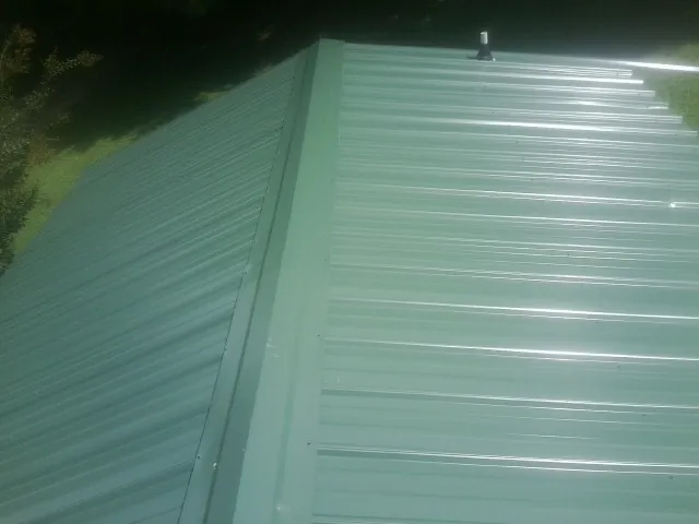 New green metal panels meeting at the ridge of a roof — Flat Roof Repair work by our crew in South Lyon