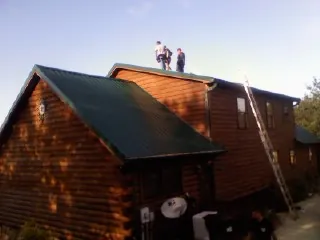 Crew on the ridge of a green metal roof on a two story log home in South Lyon