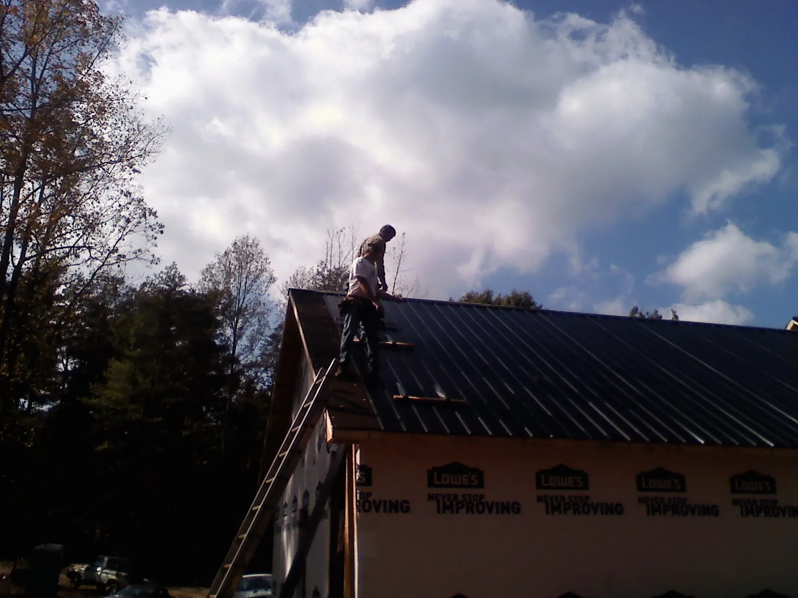 Roofer fastening dark metal panels high against a cloudy sky, from a Roof Inspection job in South Lyon