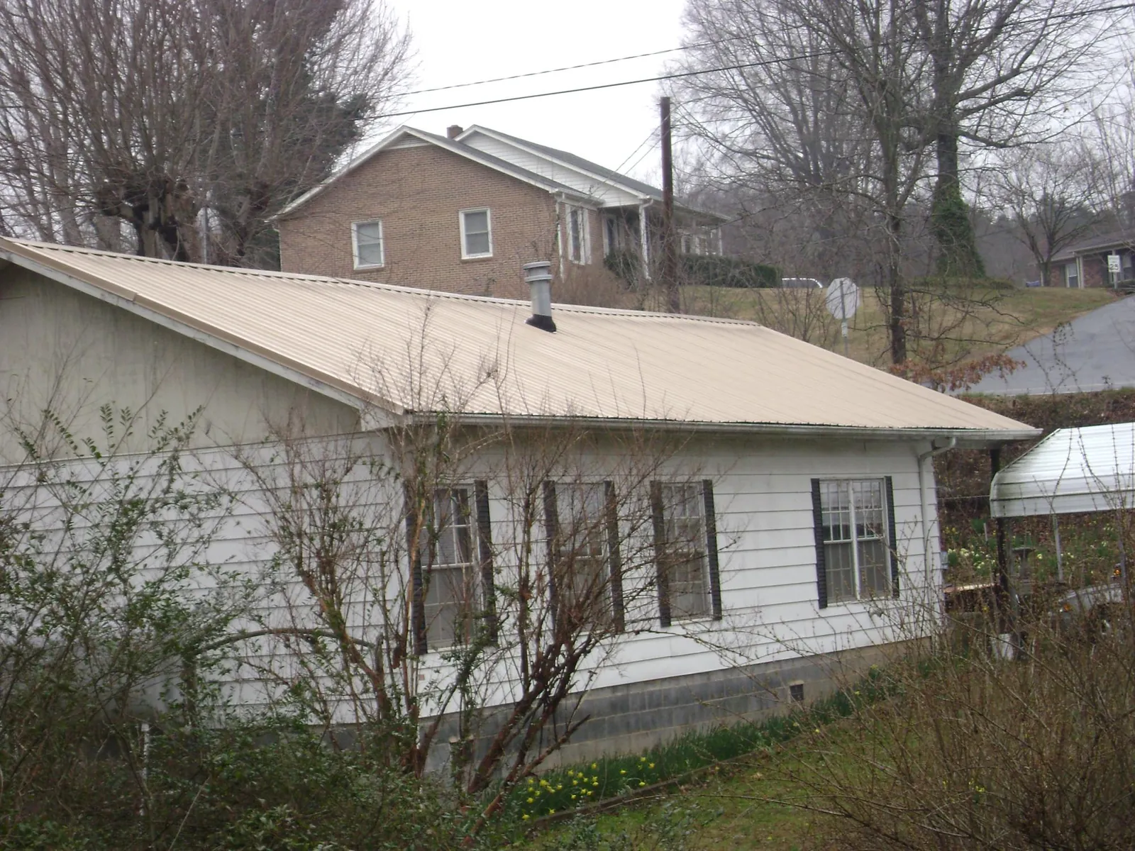 Tan metal roof on a white sided house set into a hillside — Commercial Roofing by Roofing Brothers in South Lyon